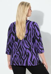 Czarna bluzka z fioletowymi paskami zebry, rękawy o długości do łokcia, boczne rozcięcia i luźny krój. Teksturowana tkanina o gładkim wykończeniu.