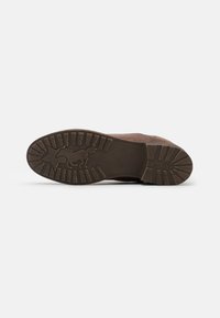 Semelle en caoutchouc marron avec un motif de semelle texturé et un logo Mustang. Tige en cuir souple d'une teinte marron légèrement plus foncée.