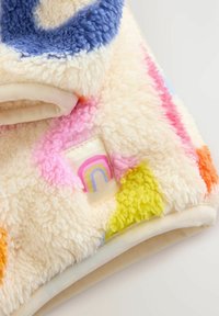 Couverture en polaire multicolore avec une texture douce. Présente des taches roses, bleues, vertes, orange et jaunes, ainsi qu'une petite patch en forme de rainbow.