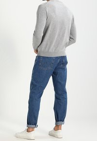 Šedý pletený svetr, modré úzké džíny s ohrnutými manžetami a bílé tenisky. Navrženo pro pohodlí s neformálním vzhledem.