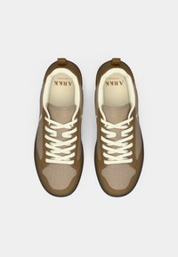 Barna és bézs sportcipők perforált felsőrésszel, krém színű fűzőkkel és fekete talppal. Megjegyezhető logó a nyelvén és sima textúra.