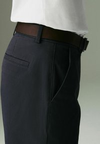 Marineblaue Hose aus glattem Stoff, mit geradem Schnitt, seitlichen Taschen und einem braunen Ledergürtel mit einer Metallschnalle.