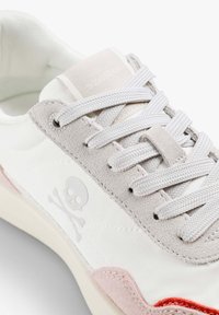 Bílé tenisky s šedými semišovými akcenty, růžovými a červenými detaily a logem lebky. Mají ploché tkaničky a strukturovaný textilní svršek.