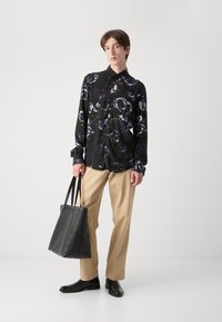 Langärmliges schwarzes Hemd mit weiß-blauem Blumenmuster; beigefarbene Hose; schwarze Ledertasche; schwarze Schuhe; glatte Textur; Knopfverschluss.