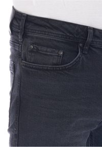 Vaqueros de mezclilla negra con un diseño clásico de cinco bolsillos, costuras visibles y un pequeño bolsillo en la parte delantera. La tela parece suave pero resistente.