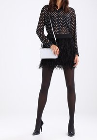 Musta, läpikuultava pilkullinen paita, höyhenillä koristeltu musta hame, mustat sukkahousut ja mustat korkokengät. Hopeanvärinen ristiin kantava laukku, jossa ketjuhihna.