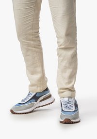 Blaue und graue Sportschuhe aus Mesh- und Wildledermaterialien, mit strukturierten Sohlen und kontrastierenden weißen Akzenten. Getragen mit beigen Hosen.