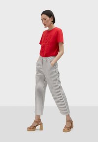 Červené tričko s krátkym rukávom a embosovaným textom, kombinované s vysokými pruhovanými nohavicami. Modelka má na sebe béžové sandále na platforme.