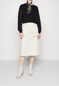 Černý pletený svetr s texturovanými rukávy, krémová midi sukně s předními kapsami, světle šedé ponožky a růžové boty na blokovém podpatku.