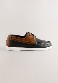 Chaussure bateau en cuir noir et marron avec semelle blanche, laçage latéral et couture blanche le long du bout sur un fond clair uni.