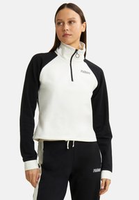 Sudadera con cremallera de un cuarto en blanco y negro con mangas ranglán, que presenta una textura suave y logo en el pecho. Dobladillo con cordón ajustable.