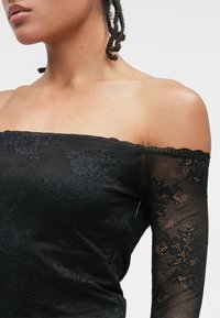 Top negru cu umeri goi, având detalii din dantelă florală, material texturat și mâneci lungi transparente cu accente de dantelă.