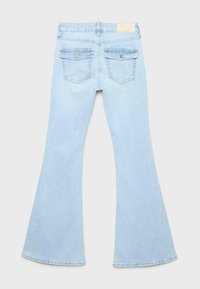 Lichtblauwe flared spijkerbroek gezien van achteren met twee knoopklepzakken en een beige merkembleem op de tailleband.