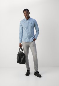 Light blue checkered button-up shirt, gray skinny jeans, black leather bag, and black shoes. Minimalistic design, tailored fit.