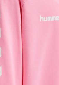 Felpa rosa con texture morbida, caratterizzata dal logo "humm" bianco e da un motivo a strisce diagonali sulla manica. Design classico con scollo rotondo.