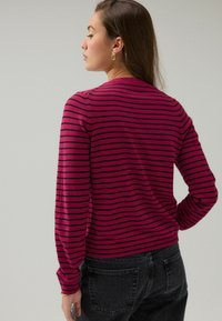 Pull en rayures rose avec des lignes noires horizontales, manches longues, col rond, tissu doux, associé à un jean foncé.
