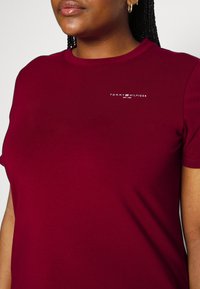 T-shirt di cotone bordeaux con collo rotondo, maniche corte e logo "TOMMY HILFIGER" bianco sulla parte sinistra del petto. Texture morbida.