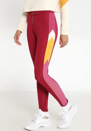 Leggings atletici rossi con motivi geometrici gialli e rosa, dettagli in rete e un tessuto liscio e elasticizzato. Abbinati a sneakers bianche.