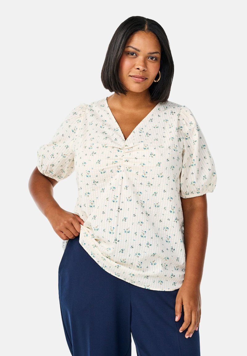 White floral blouse with puff sleeves, V-neckline, and gathered detailing. The fabric features a textured pattern and small green flowers.