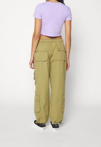 Fialové krátké tričko s krátkým rukávem, spárované s volnými olivově zelenými cargo kalhotami s několika velkými kapsami a stahovacími šňůrkami v pase.