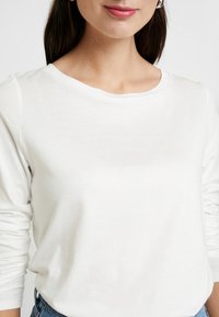 Weißes Langarmshirt mit rundem Ausschnitt, aus weichem Stoff gefertigt, mit lockerer Passform und minimalistischer Gestaltung.