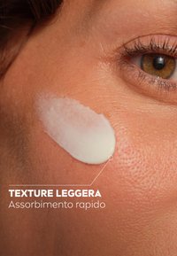 Crema bianca applicata sulla pelle, che mette in risalto una texture liscia. In primo piano, con focus sulla texture e sulle caratteristiche di assorbimento su uno sfondo marrone chiaro.