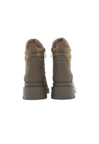 Bruna ankelstövlar med en vadderad design, fuskpälsfoder och slitstarka gummisåler. Har hängande dragflikar och sömnadsdetaljer.