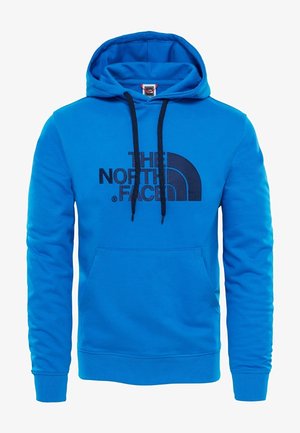 Blauwe hoodie van zacht materiaal, met een voorzak, een capuchon met koord, en een zwart logo van "The North Face" op de borst.