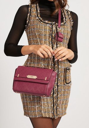 Borsa a tracolla in pelle bordeaux con motivo a logo impresso, hardware dorato e tracolla staccabile. Abbinata a un vestito in tweed multicolore e testurizzato.