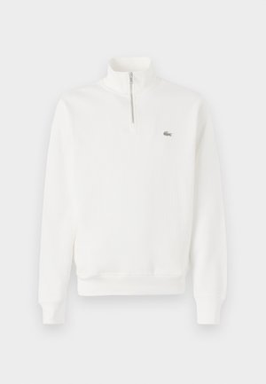 Sweatshirt branco com fecho de correr no pescoço, textura canelada, mangas compridas e um pequeno logotipo verde no lado esquerdo do peito. Apresenta uma cintura ajustada.