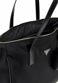 Zwarte nylon handtas met dubbele handvatten, ritssluiting en logo plaatje. Het interieur heeft een patroon voering en een extra ritszak.