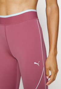 Leggings a vita alta di un profondo colore bordeaux. Realizzati in tessuto elasticizzato con accenti bianchi sui lati e una vita di colore azzurro chiaro. Presentano il logo Puma.