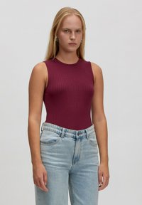 Burgunderfarbiger gerippter Bodysuit mit hohem Kragen und ärmellosem Design, kombiniert mit hellblauen, hochschnittigen Jeans. Glatte Stofftextur.