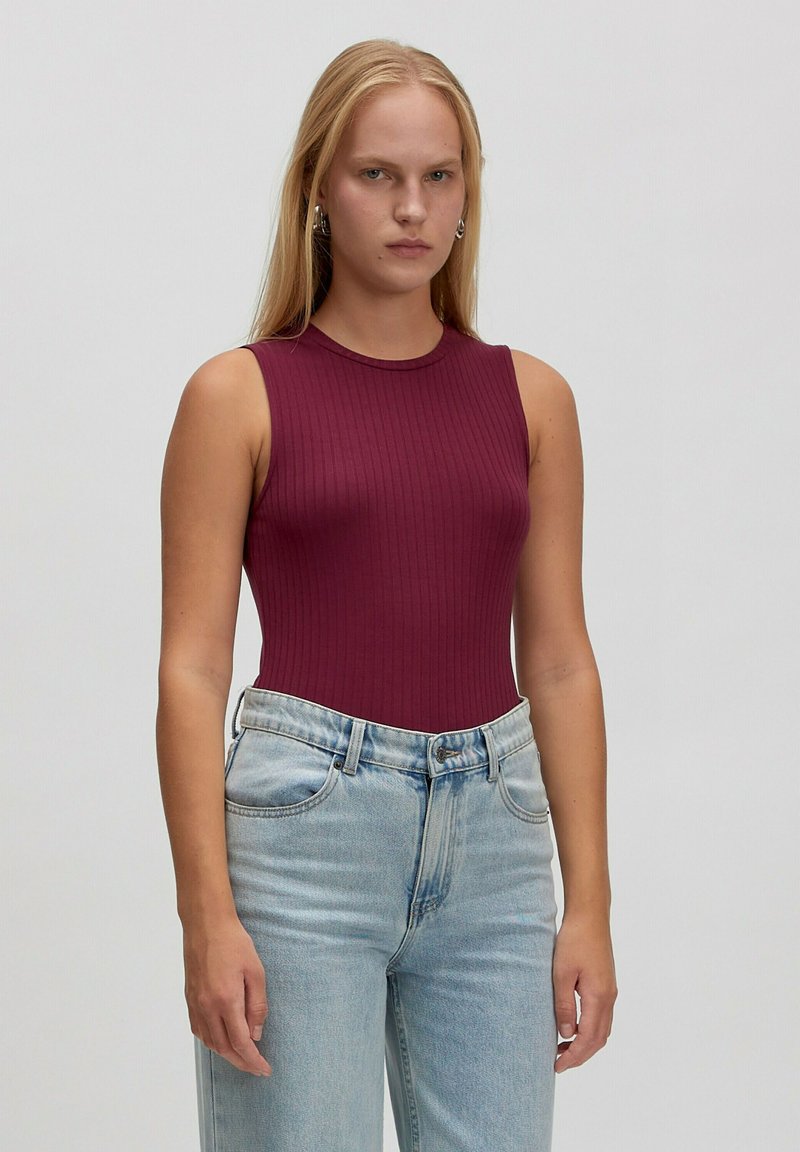Burgunderfarbiger gerippter Bodysuit mit hohem Kragen und ärmellosem Design, kombiniert mit hellblauen, hochschnittigen Jeans. Glatte Stofftextur.