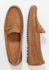 Mocassins en cuir suédé marron avec un design cousu, style à enfiler et texture douce. Semelle en caoutchouc profilée offrant adhérence et durabilité.