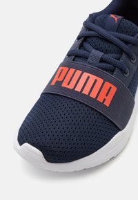 Scarpa sportiva blu navy con tomaia in mesh traspirante, suola in gomma, spessa fascia elastica a metà piede con la scritta "PUMA" in lettere arancioni.