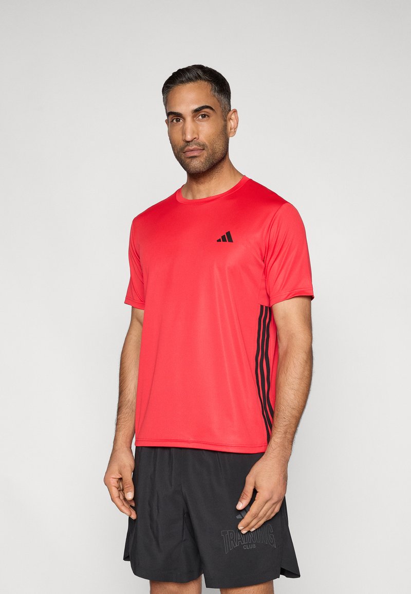 Κόκκινο αθλητικό κοντομάνικο μπλουζάκι με κοντά μανίκια, με μαύρο λογότυπο και μαύρες ριγέ λεπτομέρειες στα πλάγια. Λείο ύφασμα, κανονική εφαρμογή.