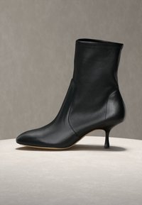 Bottine en cuir noir avec bout pointu et talon fin de hauteur moyenne sur une surface claire avec un fond neutre.