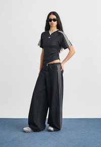 Top sport negru, cu mâneci scurte și accente albe, asortat cu pantaloni largi din denim închis la culoare, cu dungi laterale. Pantofi gri completează ținuta.