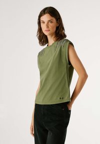 Camiseta de algodón verde oliva con mangas cortas, que presenta adornos texturizados en los hombros y un escote redondo.