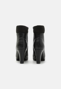 Botine negre până la gleznă, realizate din piele netedă, cu o manșetă din suede negru în contrast, având toc înalt și închidere cu fermoar lateral.