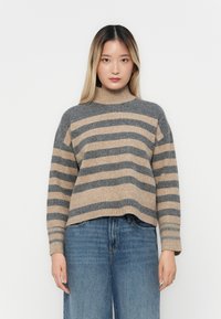 Stripet høyhalset genser i grå og beige ullblanding. Bokseformet design med ribbestrikkede mansjetter og kant. Kombinert med lyseblå vide jeans.
