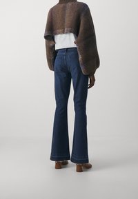Jeans a zampa d'elefante di colore blu scuro con vita alta, dotati di due tasche posteriori e orlo sfilacciato. Abbinati a un avvolgente in maglia marrone testurizzato.