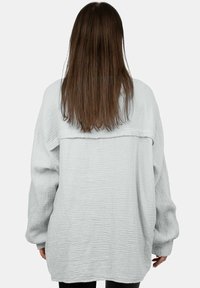 Maglione oversize grigio chiaro realizzato in tessuto testurizzato, con maniche lunghe e design con schiena aperta. Superficie liscia con motivo a griglia.