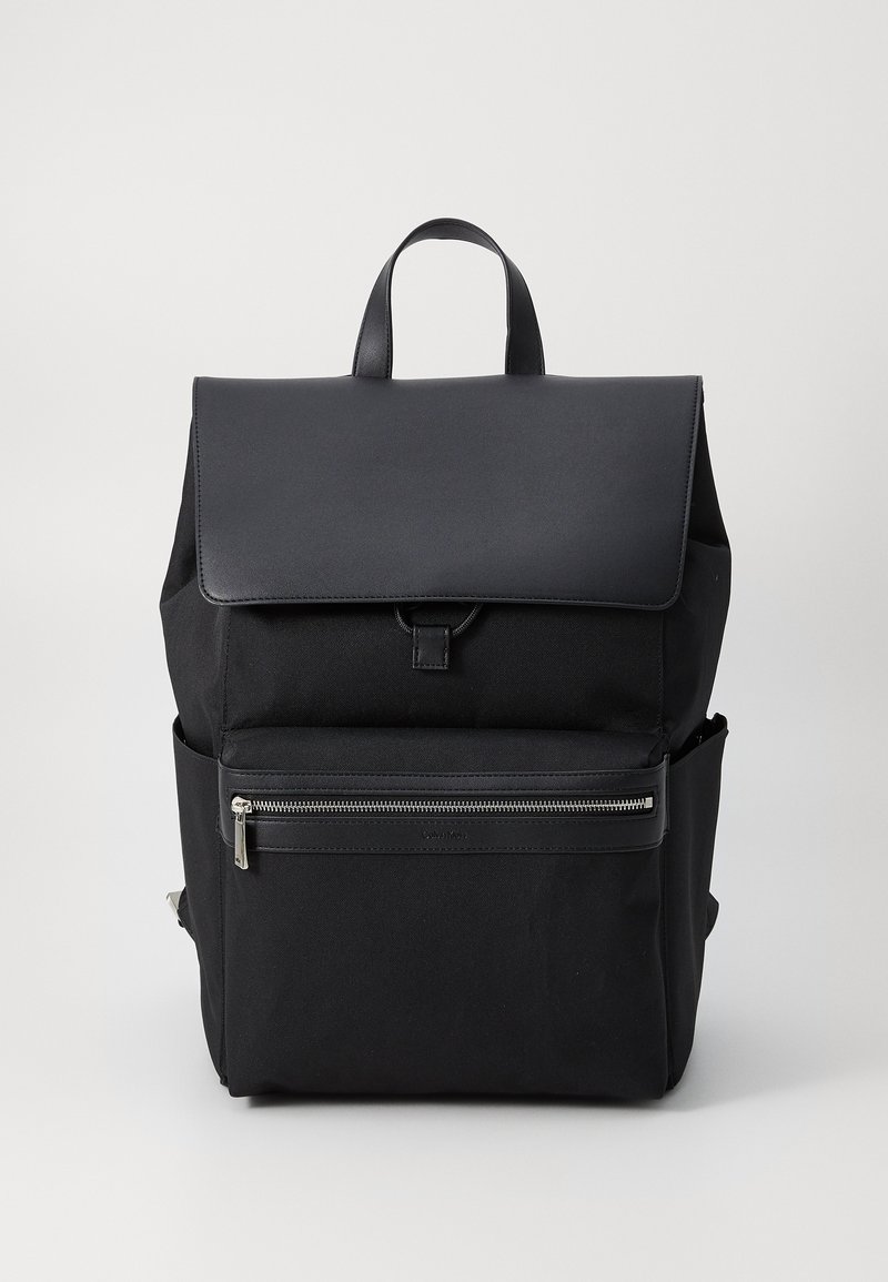 Sac à dos noir au design lisse et structuré. Il possède un rabat supérieur, une poche zippée à l'avant et deux poches latérales. Confectionné en tissu durable.