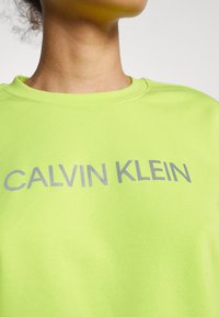 Neonowy zielony sweatshirt z okrągłym dekoltem i szarym napisem "CALVIN KLEIN". Miękka tekstura materiału, luźny kroj i czysty design.