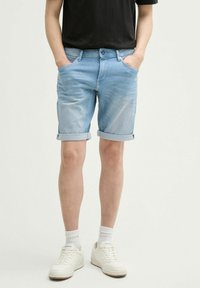 Hellblaue Denim-Shorts mit umgeschlagenen Säumen, ausgestattet mit einem klassischen Fünf-Taschen-Design und einer leicht verwaschenen Optik. Tragen Sie dazu weiße Sneakers.