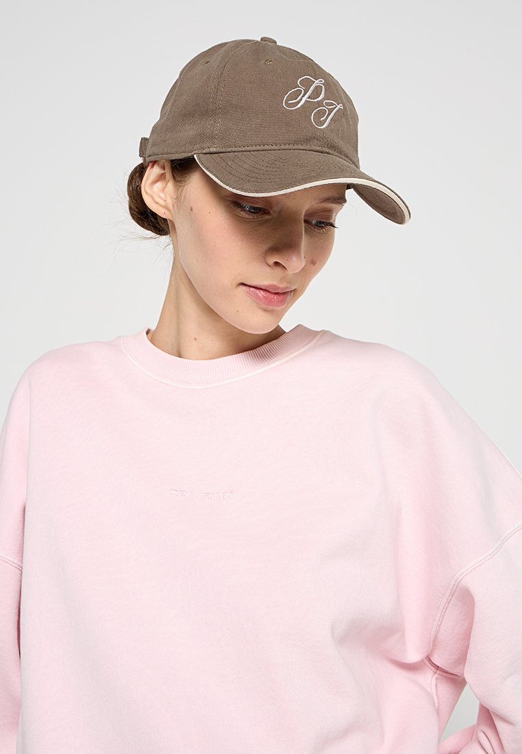 Gorra de algodón marrón con visera curvada y logo bordado en blanco, combinada con un sudadera rosa claro que presenta un nombre de marca sutilmente en relieve.
