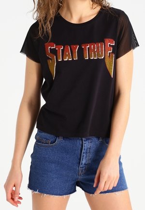 Camiseta negra de manga corta con "STAY TRUE" en letras brillantes rojas y doradas; combinada con pantalones cortos de mezclilla, con dobladillo deshilachado y color azul.
