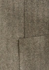 Tissu en laine chevrons marron et beige avec une poche plaquée cousue en bas à droite.